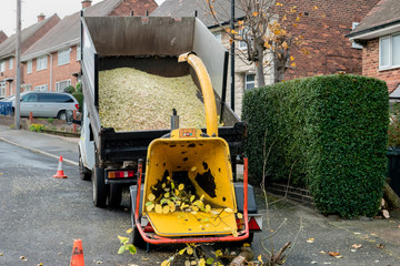 An engine-powered drum woodchipper towed behind a tipper dump truck, showing the hopper and...