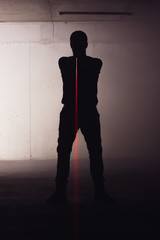Obraz premium Silhouette of an armed man holding his gun and pointing with his laser beam at a target.