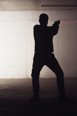 Silhouette of an armed man holding his gun and pointing with his laser beam at a target.