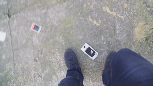 Someone is talking on a cell phone, angry and smashing on the floor and kicking parts of the phone