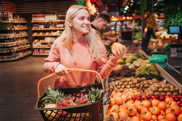 Young couple in grocery store. Woman stand in front and hold basket with orange persimmon. Cheerful...