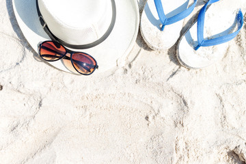 Close up straw hat, flip-flops and sunglasses  on tropical beach and white sandy. Summer vacation concept. Traveler and relax. Flat lay, top view.