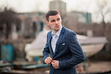 Young man businessman in jacket stands on pier against boat background