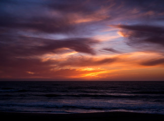 Vivid, dramatic sky over sea at sunset with blue orange gradient and dark clouds