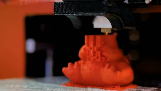 3D printer prints physical 3D model of red toy dragon with plastic wire filament at modern technology exhibition. Additive technologies, science and futuristic concept