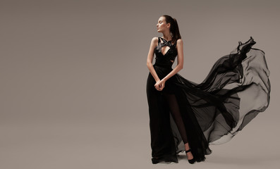 Beautiful woman in luxury evening black dress. Gray background.