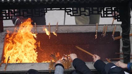 Slow motion fire and incense smoke in traditional Chinese temple, prayers put burning incense into incense burner, 4K video.