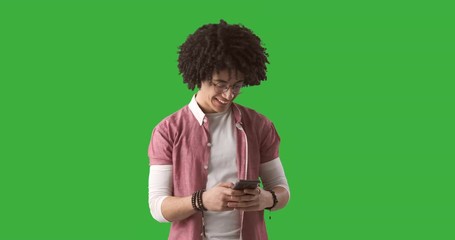 Man with curly hair text messaging on mobile phone over green chroma key background