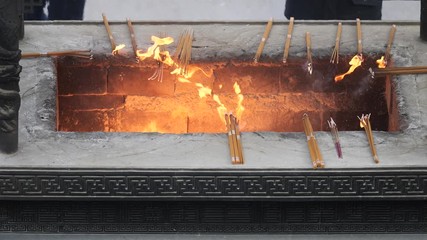 Slow motion fire and incense smoke in traditional Chinese temple, prayers put burning incense into incense burner, 4K video.