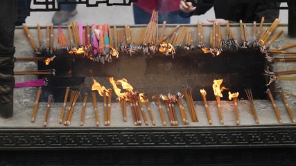 Slow motion fire and incense smoke in traditional Chinese temple, prayers put burning incense into incense burner, 4K video.