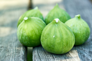A group of five freshly picked green figs on a wooden bench.