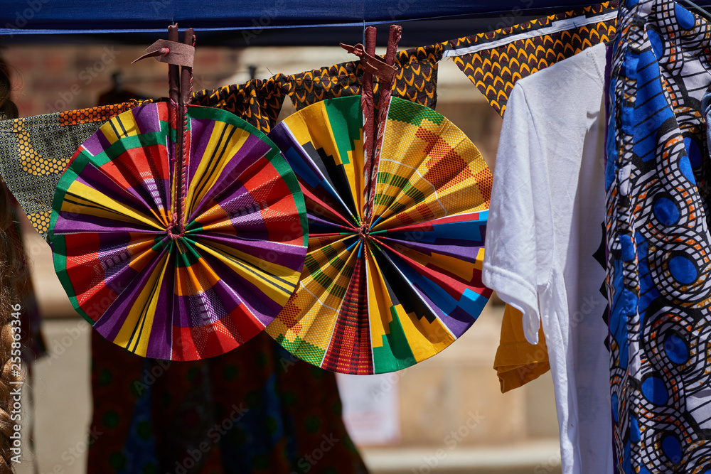 Wall mural Two colorful round hand fans hanging at a market stall on a sunny day.