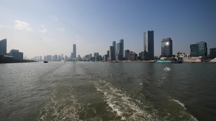 shanghai bund viewed from ferry ship, skyscrapers and landmarks with blue sky background, ships sailing on Huangpu river, Ship wake on the river, Water foam trace behind ship goes, 4K, slow motion.