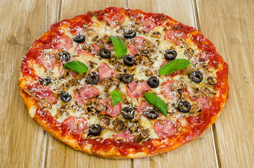 Pizza with ham, mushrooms and olives on wooden surface.