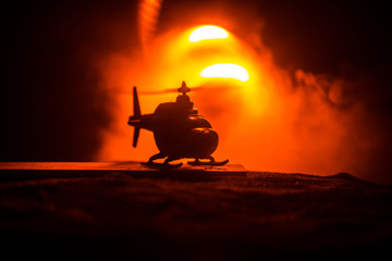 Silhouette of military helicopter ready to fly from conflict zone. Decorated night footage with helicopter starting in desert with foggy toned backlit. Selective focus.