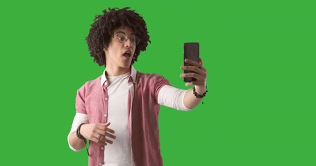 Young man with curly hair using mobile phone for video call over green chroma key background