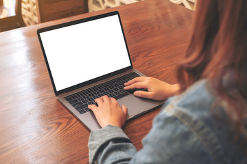 Mockup image of a woman using and typing on laptop with blank white desktop screen on wooden table in office