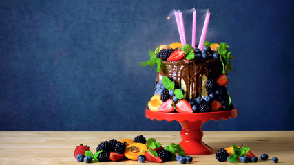 Delicious birthday chocolate drip cake decorated with fresh seasonal fruit and berries amd cancles blown out.