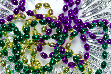 Close up view of shiny green, purple and gold Mardi Gras beads on a white crystal glass background