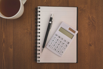 Top view workplace, Calculator and pen with notebook on wood desk background.