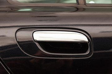 View on closed black front door with handle made from chromium of luxury car after detailing and polishing