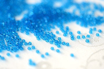 Transparent seed beads blue color scattered on a textile background close up