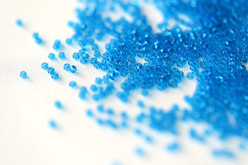 Transparent seed beads blue color scattered on a textile background close up