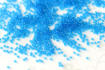 Transparent seed beads blue color scattered on a textile background close up