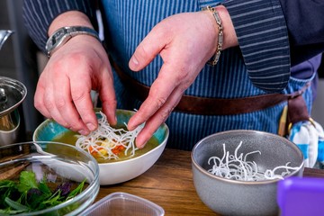 Chef decorates the soup Fo Bo from smoked catfish with cellophane noodles. Master class in the kitchen. The process of cooking. Step by step. Tutorial. Close-up