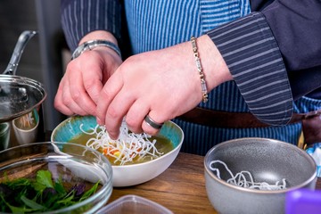 Chef decorates the soup Fo Bo from smoked catfish with cellophane noodles. Master class in the kitchen. The process of cooking. Step by step. Tutorial. Close-up