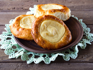 Open buns with cottage cheese (vatrushka)lying in a clay plate on a wooden table and openwork napkin.  Сloseup. Rustic Photography.