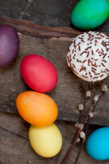 A  small Easter cake and dyed  eggs, and a willow twig on a dark wooden background.