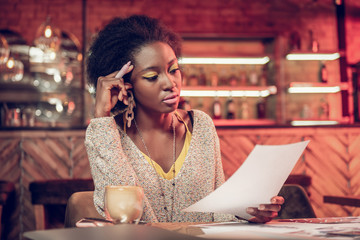 Serious Afro-American woman concernedly looking at papers in hands