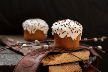 A  two small Easter cakes and a willow twig on a dark wooden background. Close up. Selective focus.