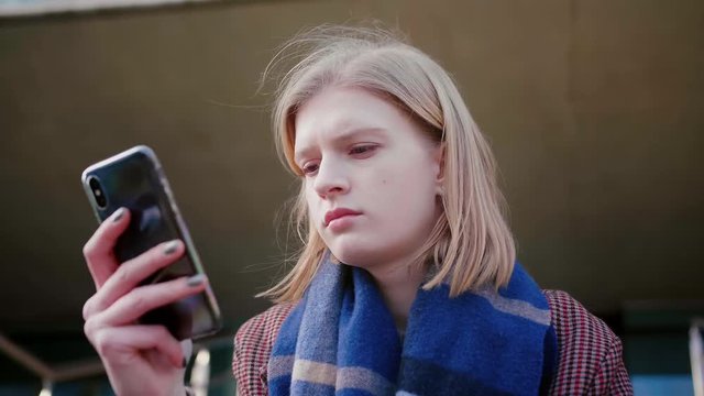 Young attractive blond girl with blue scarf using mobile phone or smartphone checking publishing post on social network website or app reading digital book encyclopedia or news feed
