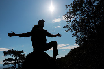 Happy and alone man silhouette on the mountain with sun and sky.