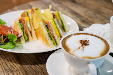 A cup of hot milk coffee  with milk and homemade sandwich (Latte coffee or Cappuccino coffee) on the wooden table in coffee shop.