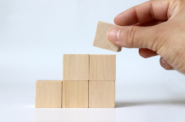 A hand piling up a wooden block with a staircase shape.
