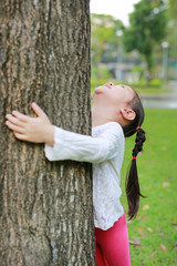 Close up of a smiling child girl embracing tree with eyes closed at the garden. 