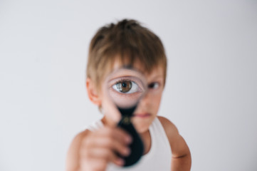 funny little caucasian boy in white tank top watching through loupe with one eye like sherlock...