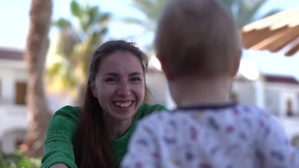 The small baby makes uncertain steps to the arms of a happy mom in slow motion