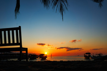 Bench with beautiful sunrise in background on tropical beach Koh rong Landscape with longtail boats while sun is going up
