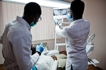 African american man patient in dental chair. Dentist office and doctor practice concept. Professional dentist helping his patient at dentistry medical. Pointing at teeth X-ray.
