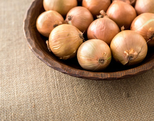 Raw organic onions on rustic wooden bowl. Table background
