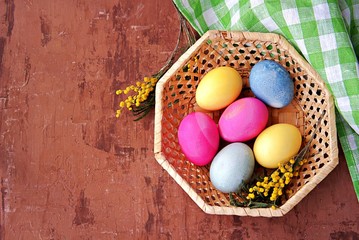 Multi-colored Easter eggs in a wicker basket on a brown background. Selective focus. Happy Easter concept.