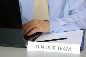 Join our team sign, man in tie sitting at desk with laptop in office, selective focus. Concept of hiring, personnel recruitment, HR manager