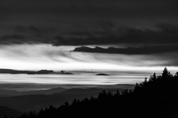 Trees silhouettes against the sky at dusk, with mountains layers in the background