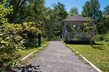 Path leading to wooden summerhouse standing among lush green trees and shrubs on bright sunny summer day. Low angle view