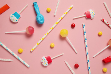 Children's birthday pink background. Scattered colorful candies, balls, candles and straws.