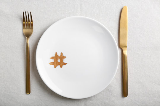 Plate with hashtag symbol and golden cutlery on light table
